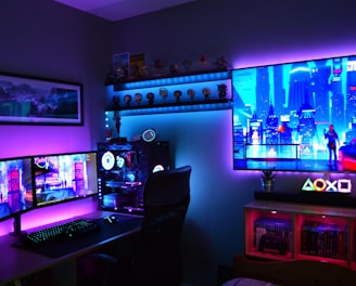 A vibrant gaming setup featuring multiple monitors displaying a cyberpunk cityscape. The room is illuminated with neon purple and blue LED lights, adding a futuristic ambiance. A custom-built PC with glowing components sits to the side, and shelves with collectible figurines are visible. A large digital screen on the wall shows an animated city scene, enhancing the immersive atmosphere.